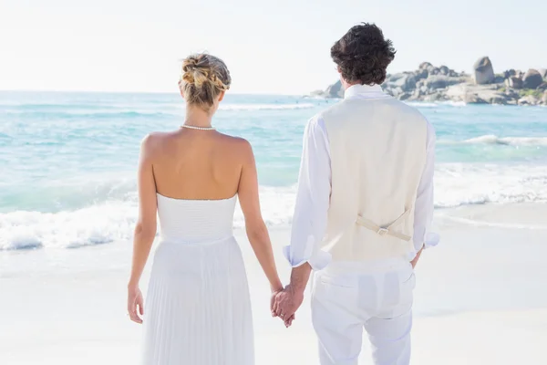 Bride and groom holding hands looking out to sea — Stock Photo, Image