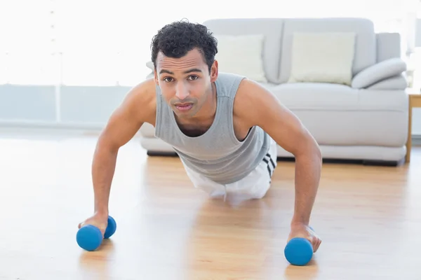 Sporty man with dumbbells doing push ups in the living room — Stock Photo, Image
