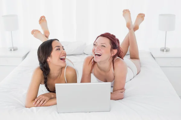 Cheerful female friends with laptop lying in bed — Stock Photo, Image