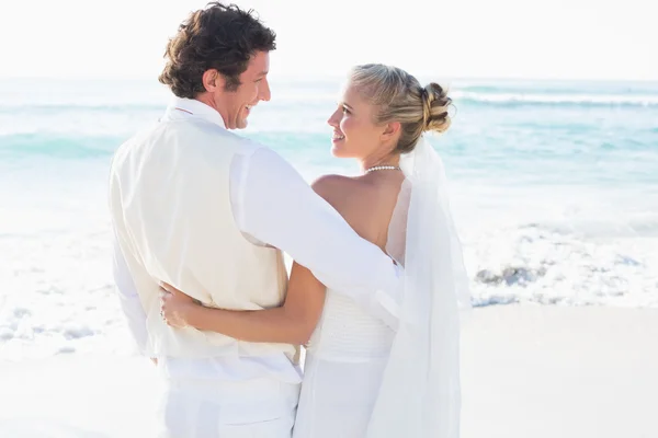Newlyweds standing by the sea smiling at each other — Stock Photo, Image