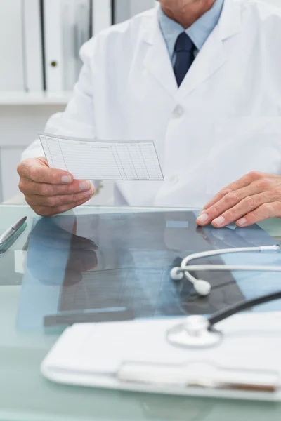 Male doctor reading a note at desk in office — Stock Photo, Image