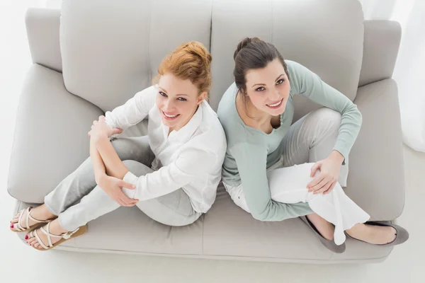 Uśmiechnięty znajomych siedzi na kanapie w salonie w domu — Zdjęcie stockowe