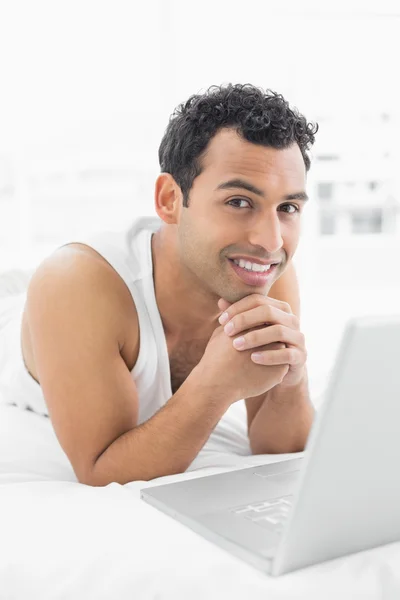 Lachende casual jonge man met laptop in bed — Stockfoto