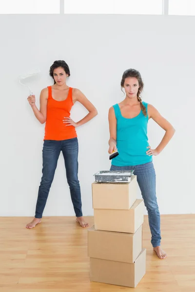 Amigos femininos com pincéis de tinta em uma nova casa — Fotografia de Stock