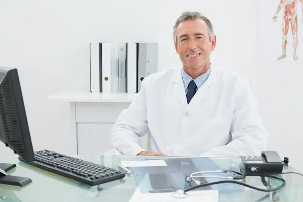 Sonriente médico varón confiado en el escritorio en la oficina —  Fotos de Stock