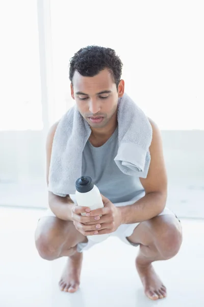 Homem com toalha em torno do pescoço segurando garrafa de água no estúdio de fitness — Fotografia de Stock