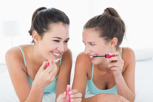 Two young female friends applying make-up in bed — Stock Photo, Image