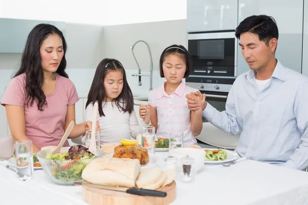 Família de quatro dizendo graça antes da refeição na cozinha — Fotografia de Stock