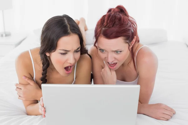 Shocked female friends looking at laptop in bed — Stock Photo, Image