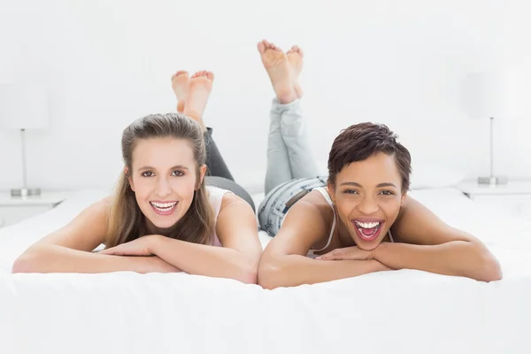 Vrolijke jonge vrouwelijke vrienden liggend in bed — Stockfoto