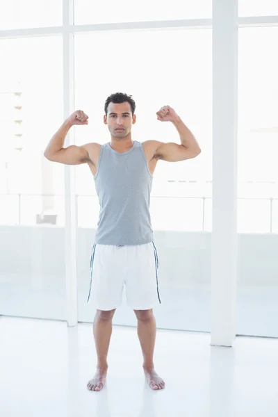 Fit young man flexing muscles in fitness studio — Stock Photo, Image