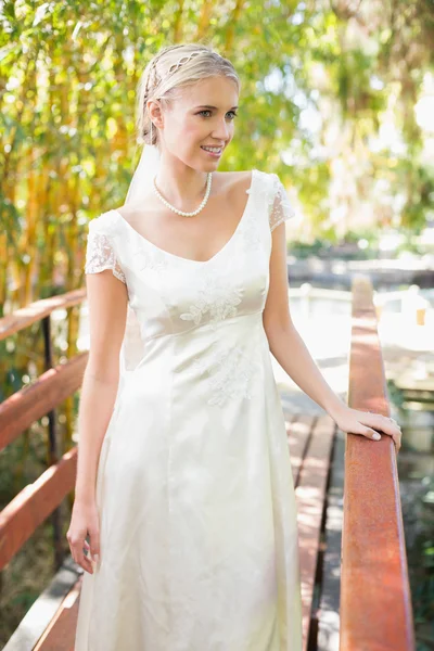 Content blonde bride in pearl necklace standing on a bridge — Stock Photo, Image