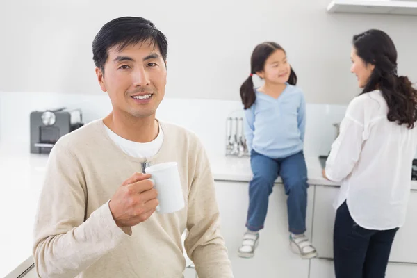 Sonriente hombre sosteniendo la taza de café con la familia en el fondo — Foto de Stock