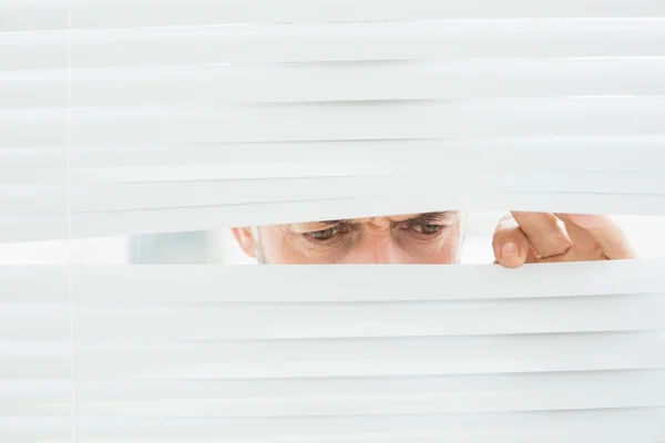 Close-up van een volwassen zakenman gluren door blinds — Stockfoto