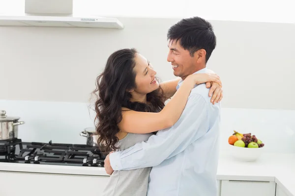 Vista lateral de um homem abraçando a mulher na cozinha — Fotografia de Stock