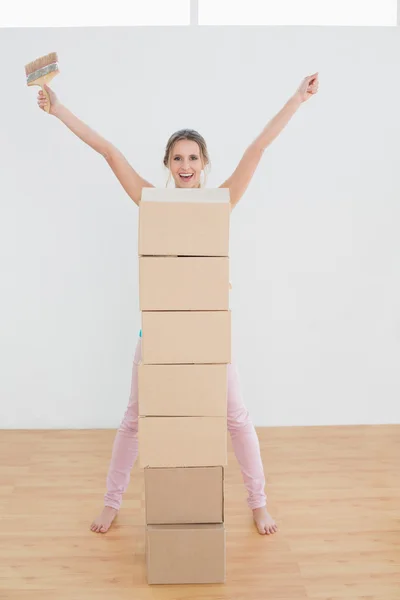 Woman with stack of boxes and paintbrush in a new house — Stock Photo, Image