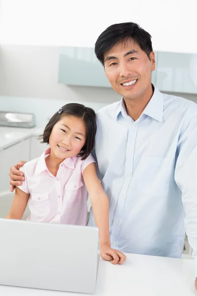 Sonriente padre y joven hija con portátil en la cocina — Foto de Stock