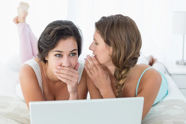 Relaxed female friends with laptop gossiping in bed — Stock Photo, Image