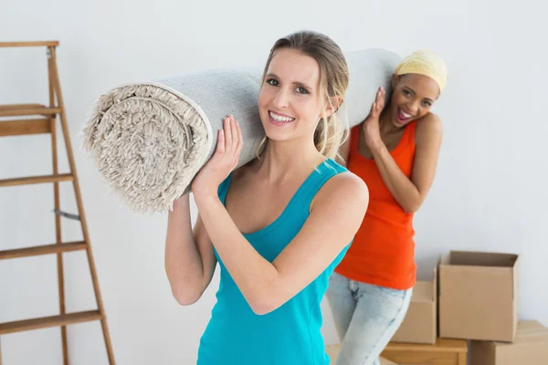 Female friends carrying rolled rug after moving in a house — Stock Photo, Image