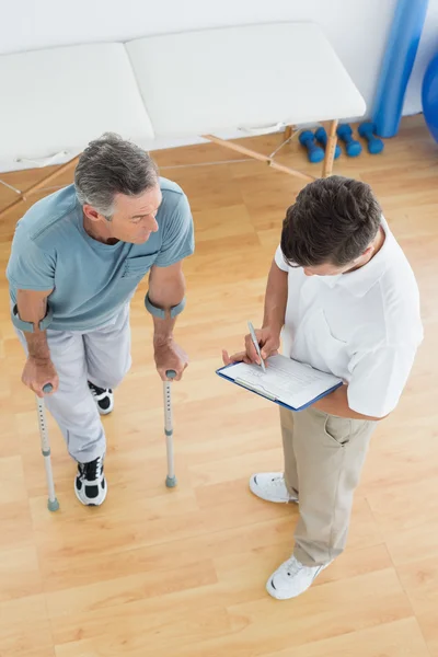 Therapist discussing reports with a disabled patient in gym hospital — Stock Photo, Image