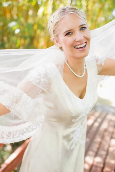 Ziemlich glückliche blonde Braut hält ihren Schleier heraus und lächelt in die Kamera — Stockfoto