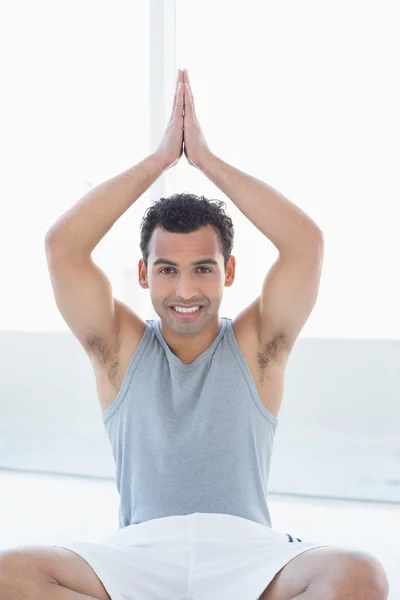Smiling young man sitting with joined hands over head — Stock Photo, Image