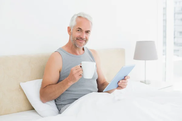 Homem maduro com tablet digital e mesa de café na cama — Fotografia de Stock