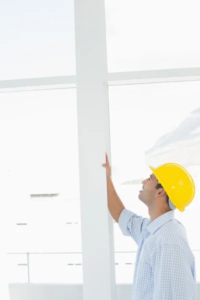 Handyman in yellow hard hat examining window in office — Stock Photo, Image