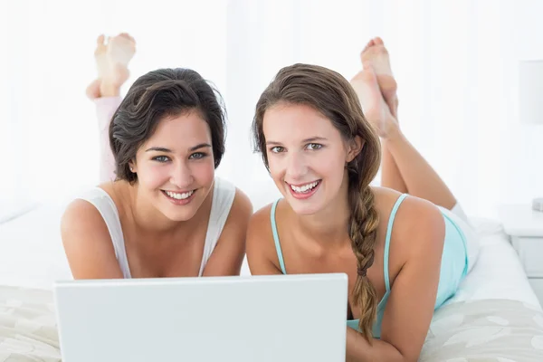 Felices amigas relajadas usando laptop en la cama —  Fotos de Stock