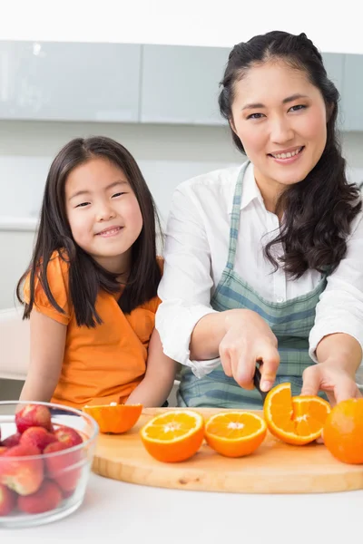 Mujer con su hija pequeña cortando fruta en la cocina —  Fotos de Stock