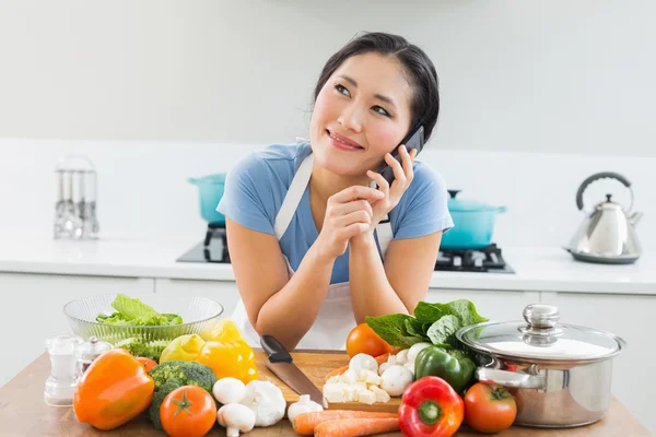 Mujer usando teléfono móvil delante de las verduras en la cocina — Foto de Stock