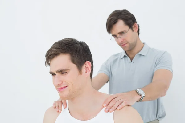 Fisioterapeuta masculino masajeando un hombro de hombre joven —  Fotos de Stock