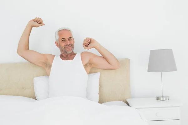 Dojrzały człowiek uśmiechający się wyciąganie broni w łóżku — Zdjęcie stockowe