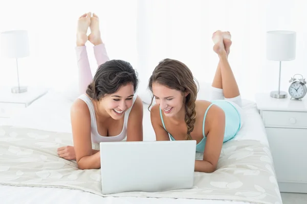 Felices amigas relajadas usando laptop en la cama —  Fotos de Stock