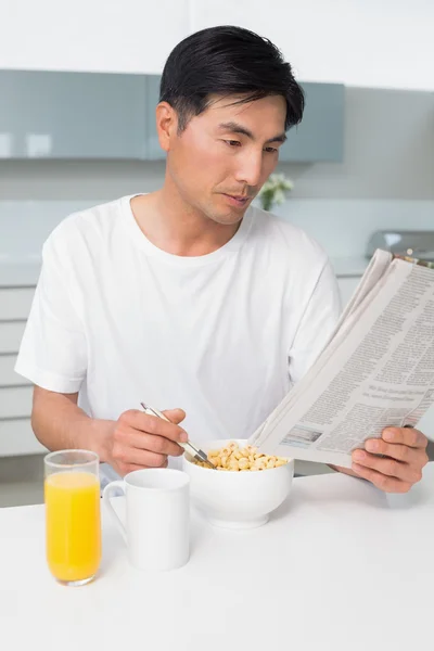 Homem sério ter cereais enquanto lê jornal na cozinha — Fotografia de Stock