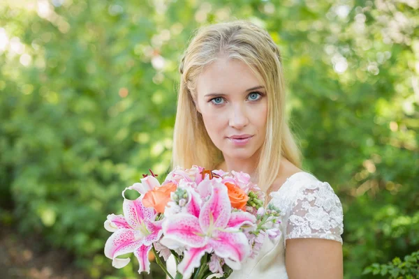 Blonde bride holding big bouquet smiling at camera — Stock Photo, Image