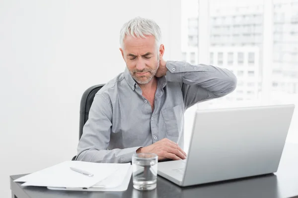 Hombre que sufre de dolor de cuello mientras usa el ordenador portátil en el escritorio de la oficina —  Fotos de Stock