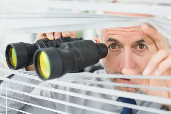 Reifer Geschäftsmann blickt mit Fernglas durch Jalousien — Stockfoto