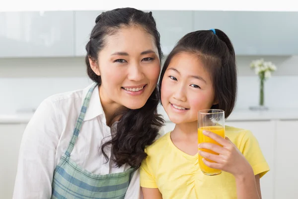 Girl holding orange juice with her mother in kitchen — Stock Photo, Image