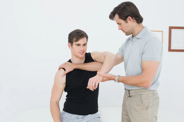 Fisioterapeuta masculino examinando un brazo de hombre joven — Foto de Stock