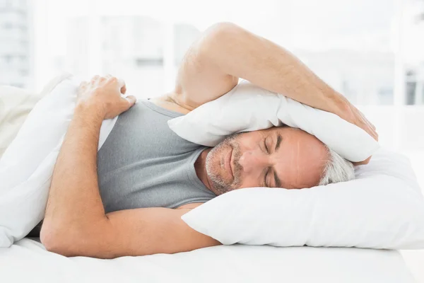 Sleepy man covering ears with pillow in bed — Stock Photo, Image