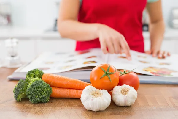 Sección media de una mujer con libro de recetas y verduras —  Fotos de Stock