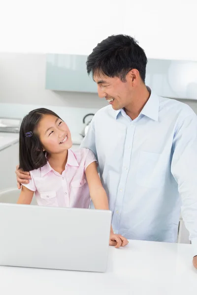 Smiling father with young daughter using laptop in kitchen — Stock Photo, Image