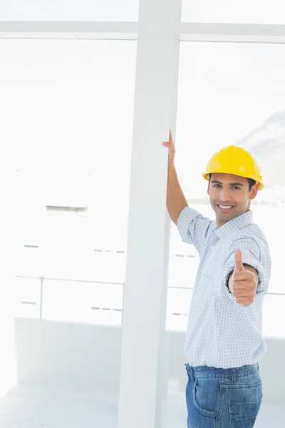 Handyman em chapéu duro amarelo gesticulando polegares no escritório — Fotografia de Stock