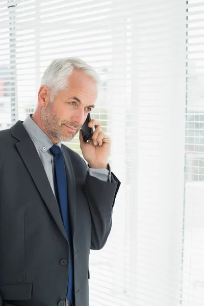 Businessman peeking through blinds while on call in office — Stock Photo, Image