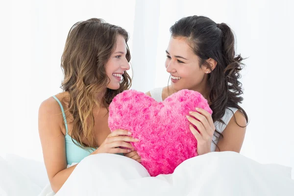 Amis féminins avec oreiller en forme de coeur au lit — Photo