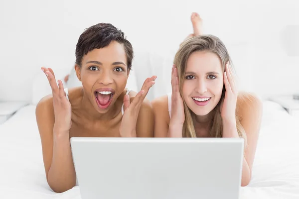 Shocked young female friends with laptop in bed — Stock Photo, Image