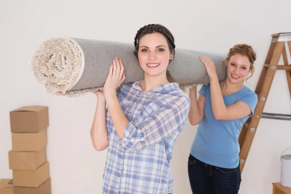 Female friends carrying rolled rug after moving in a house — Stock Photo, Image