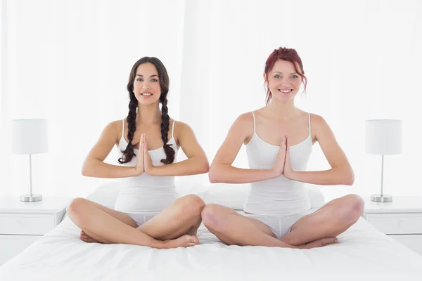 Two young women sitting with joined hands on bed — Stock Photo, Image