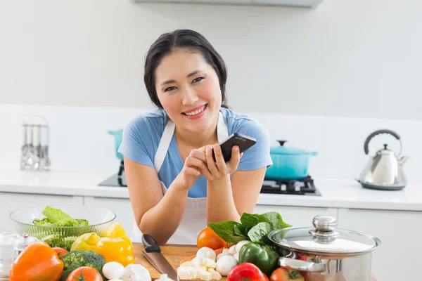 Lachende vrouw voor SMS-berichten voor groenten in de keuken — Stockfoto